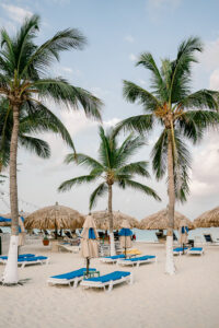 Beach chairs with thatched huts and palm trees on the beach in Aruba