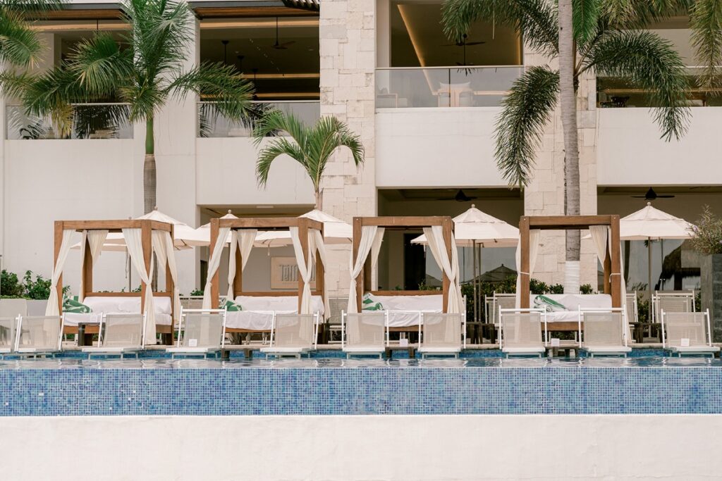 Luxury poolside cabanas at Hyatt Ziva Puerto Vallarta, featuring white canopy beds, lounge chairs, and umbrellas beside a sparkling infinity pool, surrounded by palm trees and modern resort architecture.