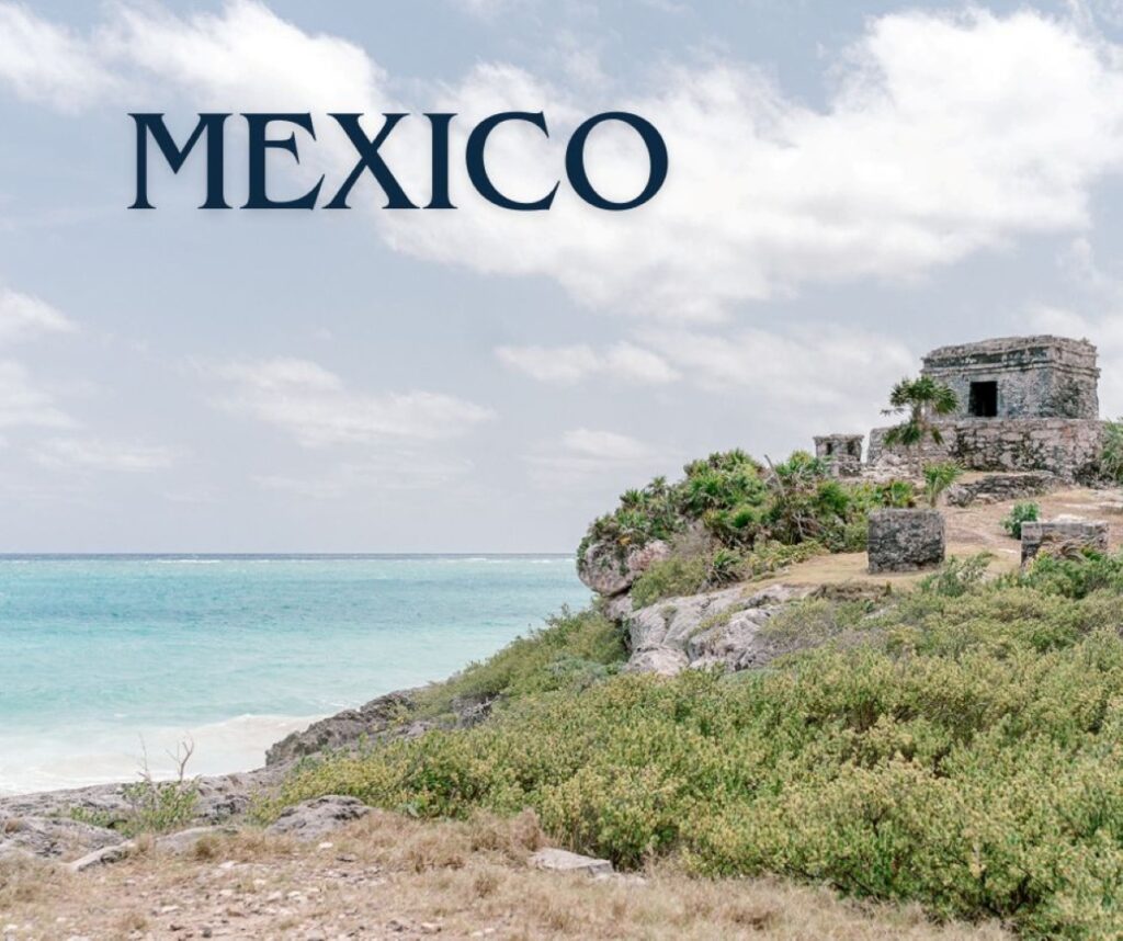 Scenic coastal view of the Tulum ruins in Mexico, featuring a stone Mayan structure perched on a cliff overlooking the turquoise waters of the Caribbean Sea under a partly cloudy sky