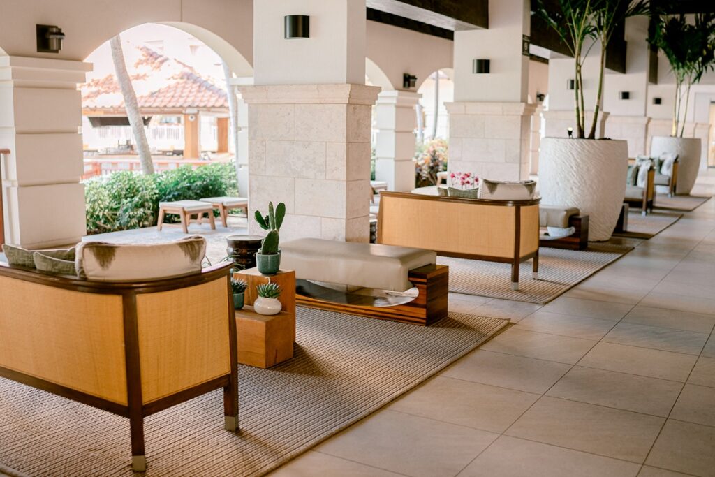 A serene open-air lobby at the Hyatt Regency Aruba, featuring modern tropical lounge seating, potted plants, and soft natural lighting—offering guests a relaxing and stylish welcome to paradise.