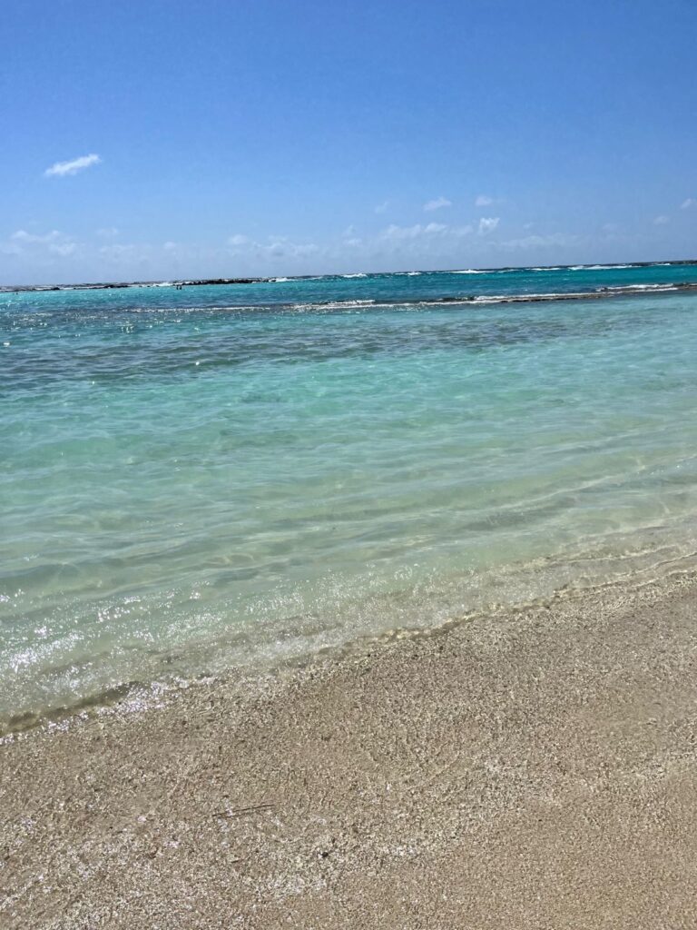 Crystal-clear turquoise waters gently lapping against the soft sandy shore at Baby Beach in Aruba, with shallow waves and a vibrant blue sky overhead—perfect for swimming, snorkeling, and relaxing in paradise.