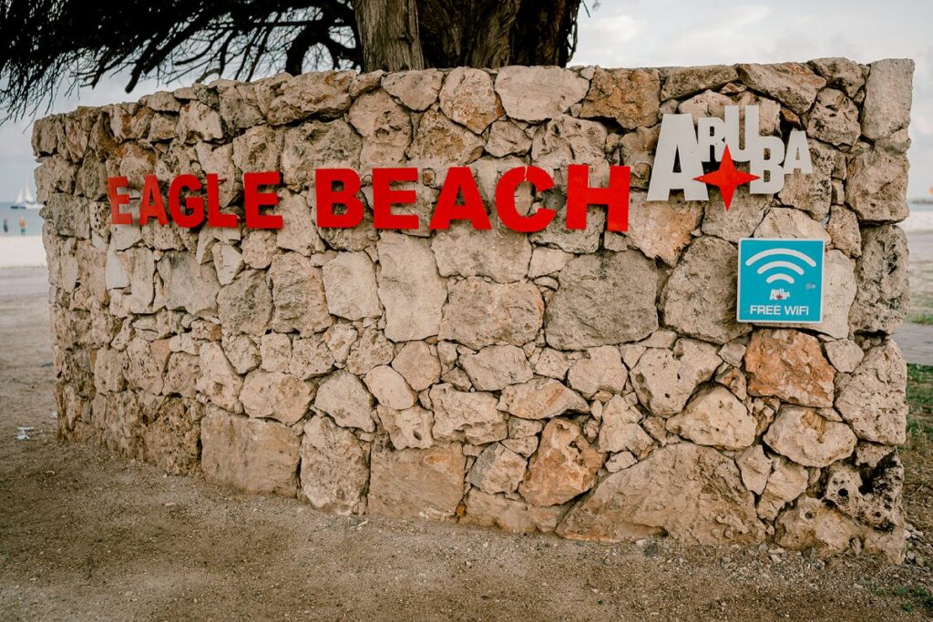 A rustic stone sign at Eagle Beach in Aruba, with bold red lettering and a metal Aruba logo, offering visitors free WiFi—welcoming beachgoers to one of the island’s most famous and scenic stretches of shoreline.