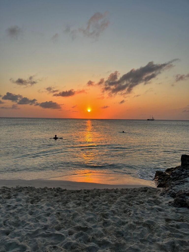 A serene sunset on the beach in Aruba. A glowing orange sky and golden sun reflecting off the calm ocean wave.