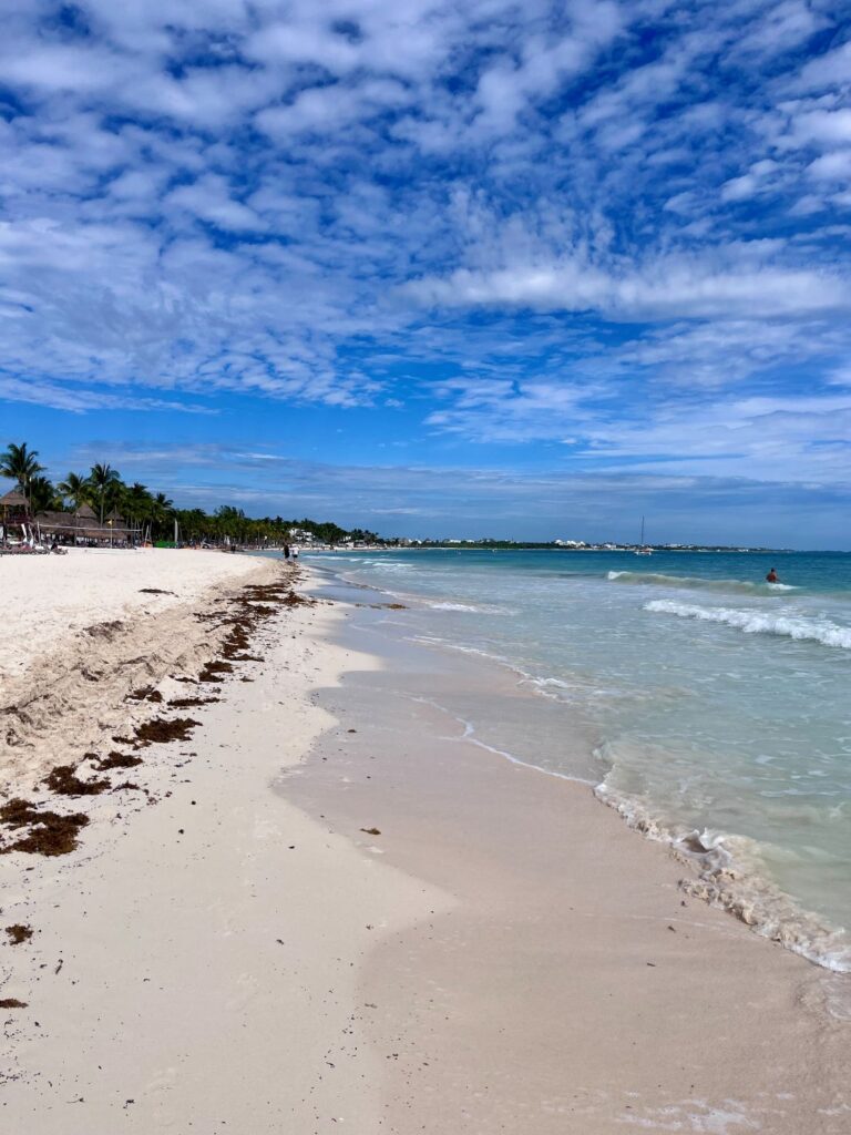 White-sand beach at Secrets Maroma Beach with turquoise water, palm trees, and a partly cloudy blue sky in Riviera Cancun.