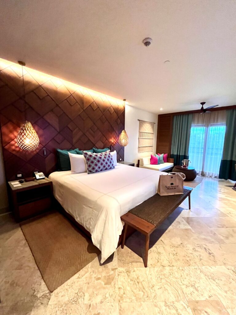 Spacious guest room at Secrets Maroma Beach featuring a king bed, woven accent wall, sitting area, and balcony doors