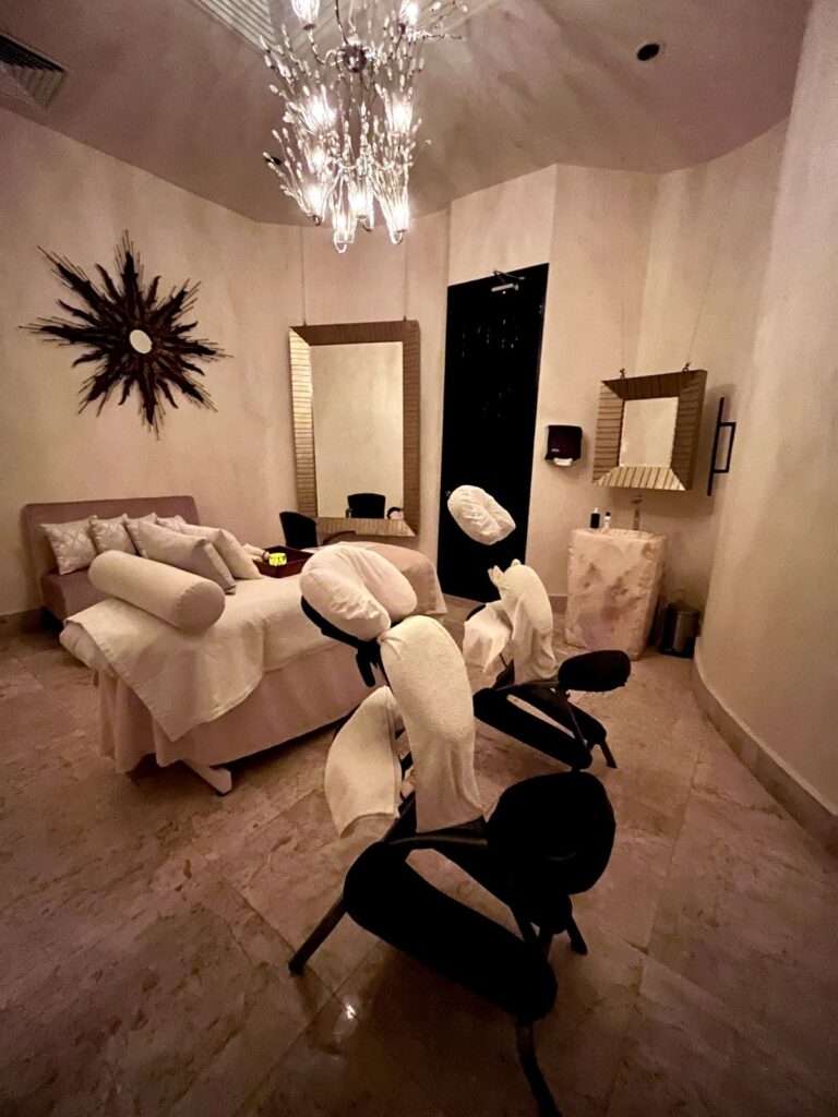 Luxury spa treatment room with massage table, chandelier lighting, and massage chairs at Secrets Maroma Beach Riviera Cancun