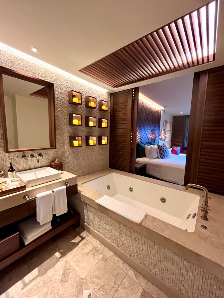 Elegant spa-style bathroom at Secrets Maroma Beach with deep soaking tub, warm lighting, and open-concept bedroom layout