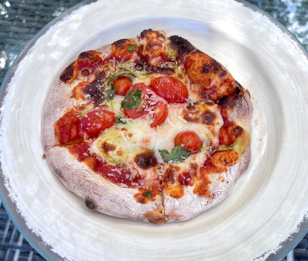Wood-fired margherita pizza topped with melted mozzarella, cherry tomatoes, fresh basil, and grated parmesan, served at Secrets Maroma Beach Riviera Cancun.
